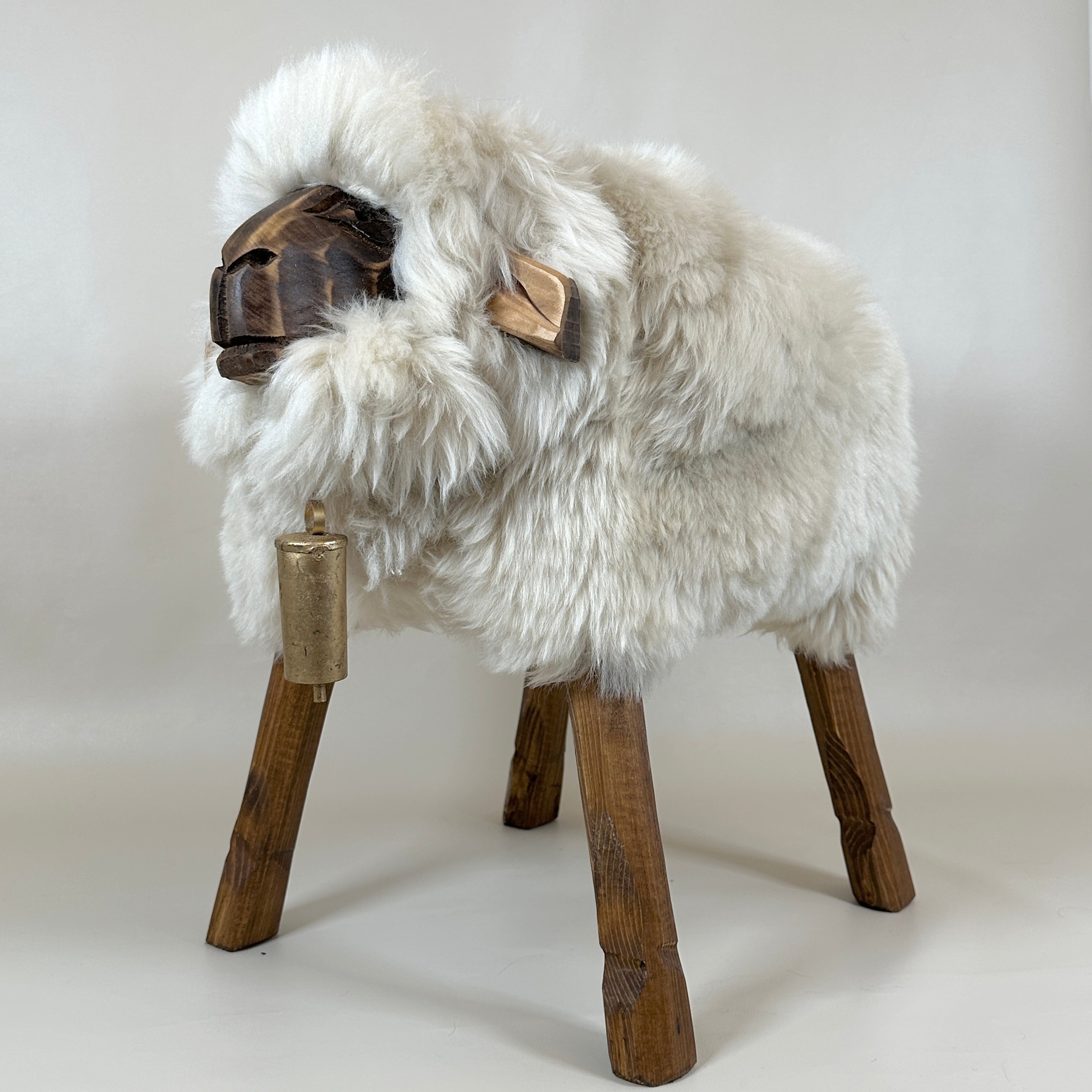 Carica video: Video zeigt Schafhocker Tina in champagner-beiger Farbe, rotiert langsam um 360 Grad, zeigt alle Seiten des handgefertigten Hockers, vier Holzbeine sichtbar, flauschiges echtes Schaffell als Sitzfläche, neutrale Hintergrundbeleuchtung, Produktpräsentation ohne Ton